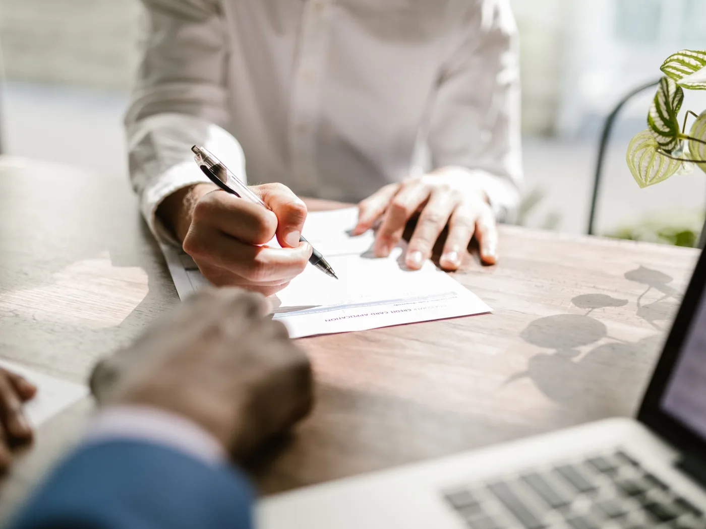 Close-up of a person signing a document at a sunlit table